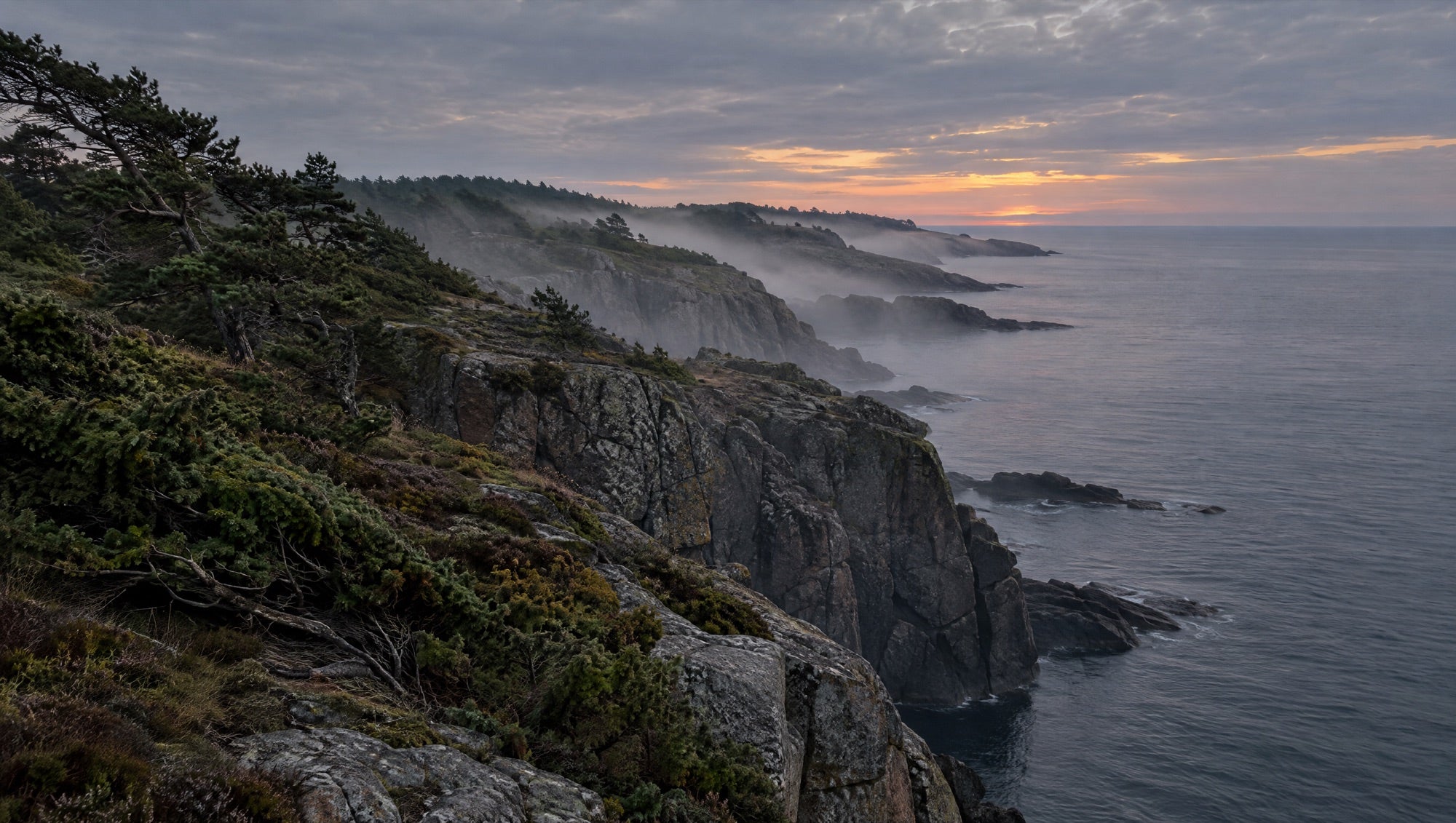 The granite cliffs of Bornholm at dusk, with sea mist over the Baltic