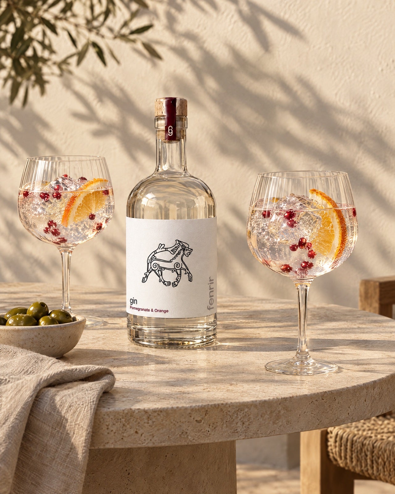 Fenrir gin and two balloon glasses of gin and tonic on a stone terrace table in early evening sun