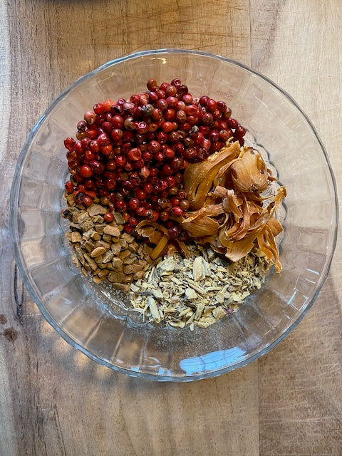 Pomegranate seeds, orange peel and dried botanicals in a glass bowl before distilling