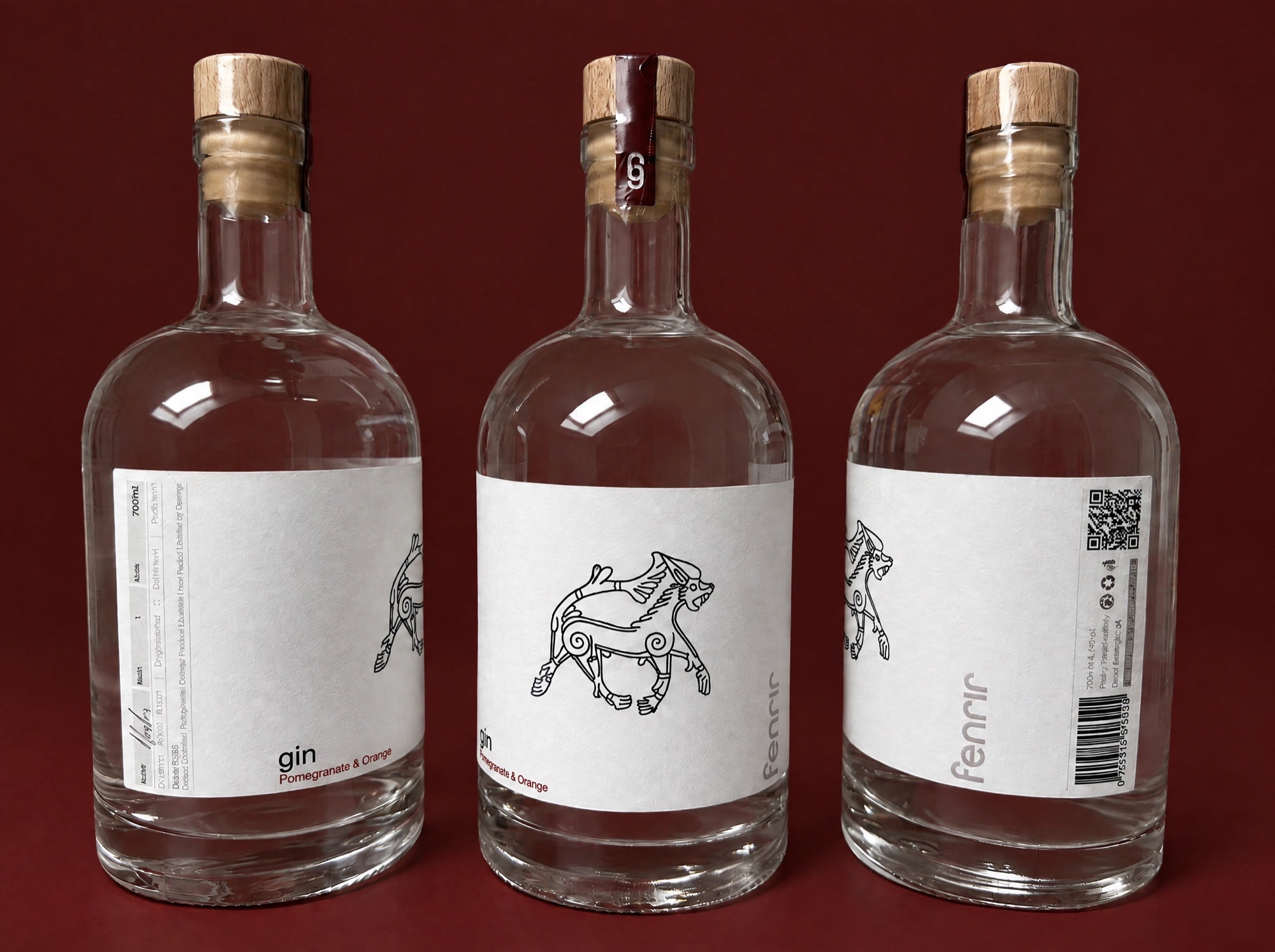 Three bottles of Fenrir gin, showing the front, side and back of the label, on a deep oxblood background
