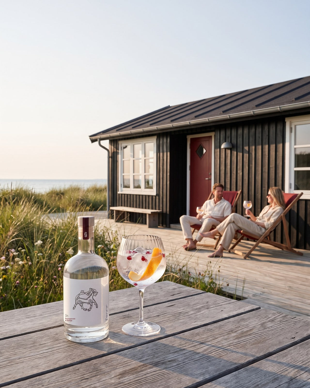 Fenrir gin and a gin and tonic on a garden table at a Danish summer house, two friends in deck chairs behind