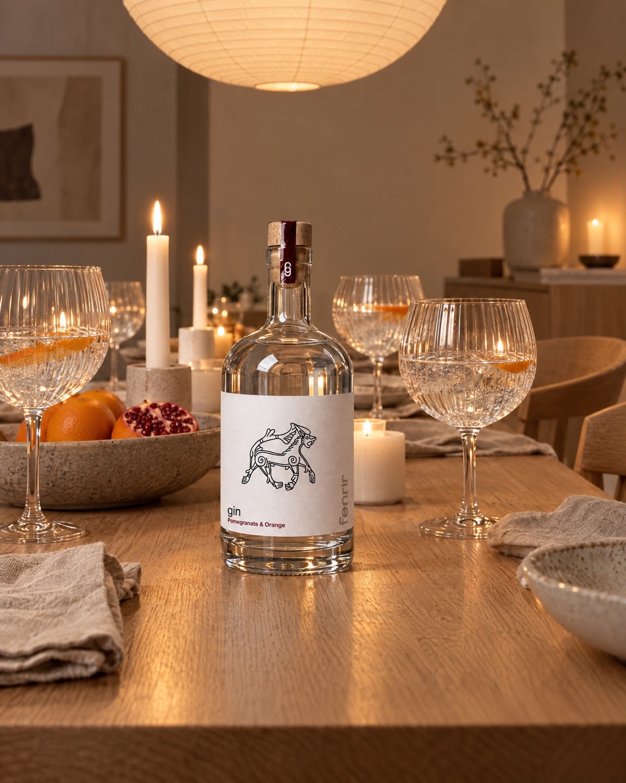 Fenrir gin on a long oak dining table after dinner, with candles, glasses and a bowl of oranges